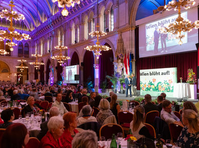 Blick in den vollbesetzten großen Festsaal des Wiener Rathauses. An den Tischen sitzen Menschen, im Vordergrund eine Bühne auf der gerade jemand von Karl Ploberger interviewt wird. Alles ist prächtig mit Blumen in den unterschildichsten Farben geschmückt.