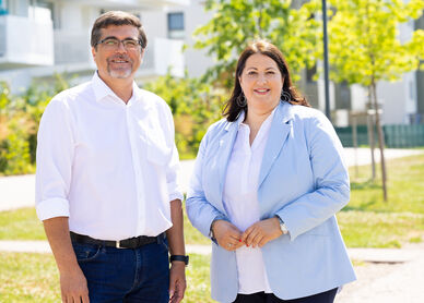 Leiter der MieterHilfe der Stadt Wien Christian Bartok steht neben Vizebürgermeisterin und Wohnbaustadträting Kathrin Gaál. Die beiden sind sommerlich gekleidet, Gaál in einem hellblauen Blazer über einer weßen Bluse, Christian Bartok mit Jean und weißem Hemd, bei dem die Ärmel bis zu den Ellenbogen hochgekrempelt sind. Das Wetter ist sonnig und freundlich.