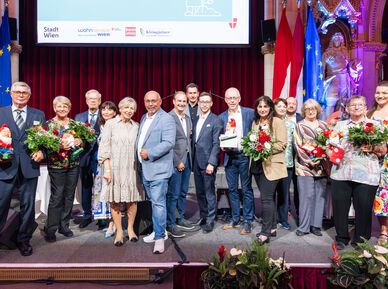Alle 16 Preisträger*innen des heurigen Kleingartenpreises versammelt auf der Bühne mit Blumensträußen. 