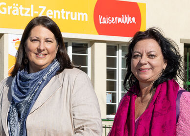 Viezbürgermeisterin Gall steht mit wohnpartner-Bereichsleiterin Claudia Huemer vor einem Gebäude. Über dem Eingangsportal ist der Schriftzug Grätzl-Zentrum Kaisermühlen zu lesen..