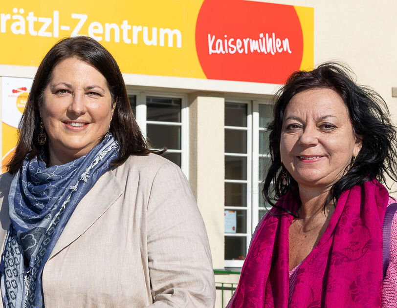 Viezbürgermeisterin Gall steht mit wohnpartner-Bereichsleiterin Claudia Huemer vor einem Gebäude. Über dem Eingangsportal ist der Schriftzug Grätzl-Zentrum Kaisermühlen zu lesen..