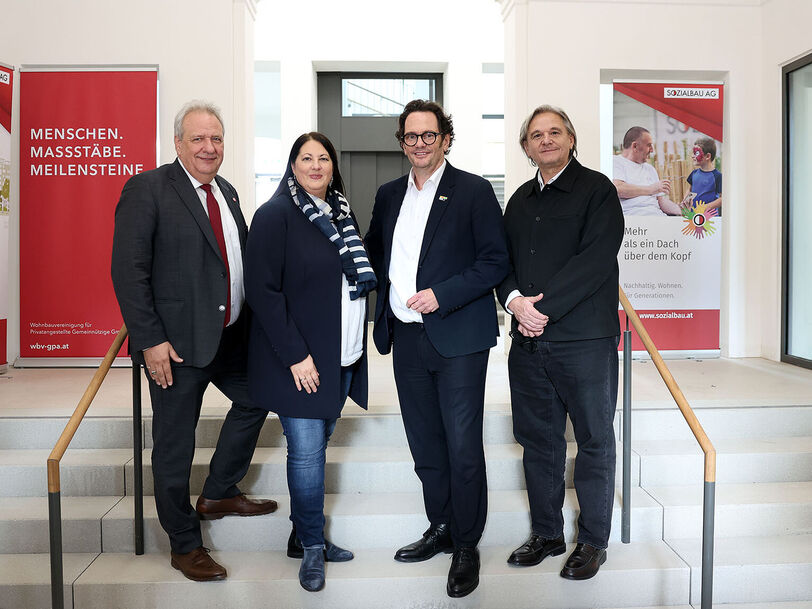 Drei Männer und eine Frau stehen auf Stufen in einem alten aber frischrenovierten Stiegenhaus.