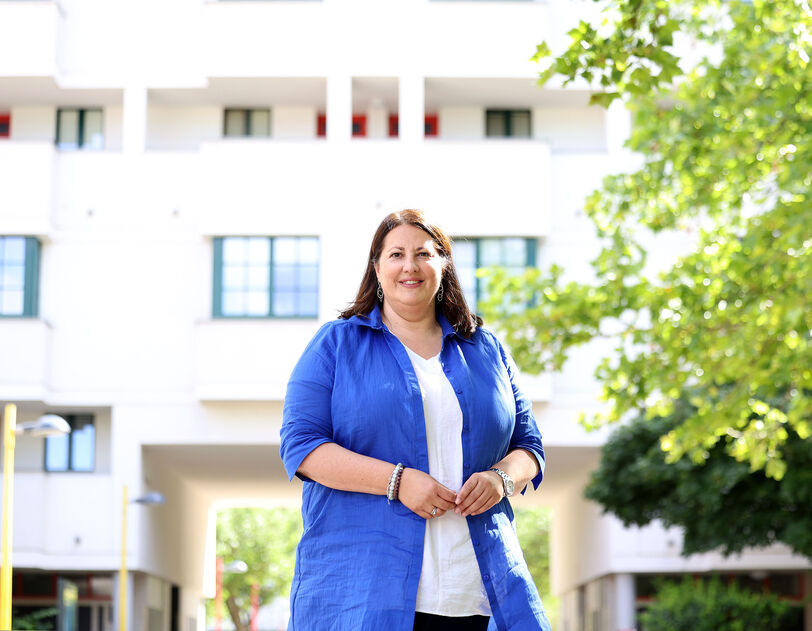 Vizebürgermeisterin Kathrin Gaál steht vor einem neuen Gebäude, sie trägt ihre die brauen Haare offen und ist mit einer blauen langen Bluse über weißem T-Shirt bekleidet.