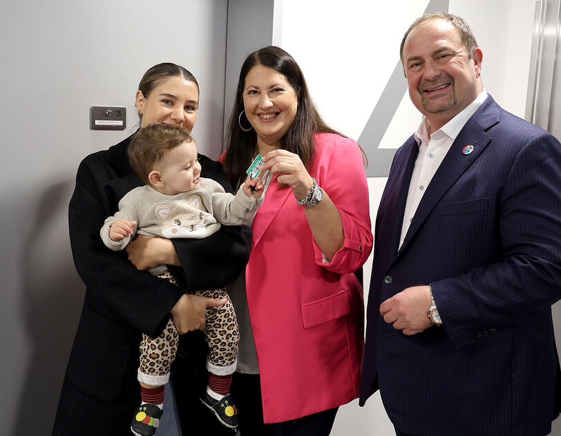 Vizebürgermeisterin und Wohnbaustadträtin Kathrin Gaál und Bezirksvorsteher Alexander Nikolai in der neuen Wohnhausanlage übergeben einer Frau mit Baby am Arm die Schlüssel zu ihrer neuen Wohnung.