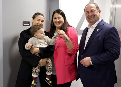 Vizebürgermeisterin und Wohnbaustadträtin Kathrin Gaál und Bezirksvorsteher Alexander Nikolai in der neuen Wohnhausanlage übergeben einer Frau mit Baby am Arm die Schlüssel zu ihrer neuen Wohnung.