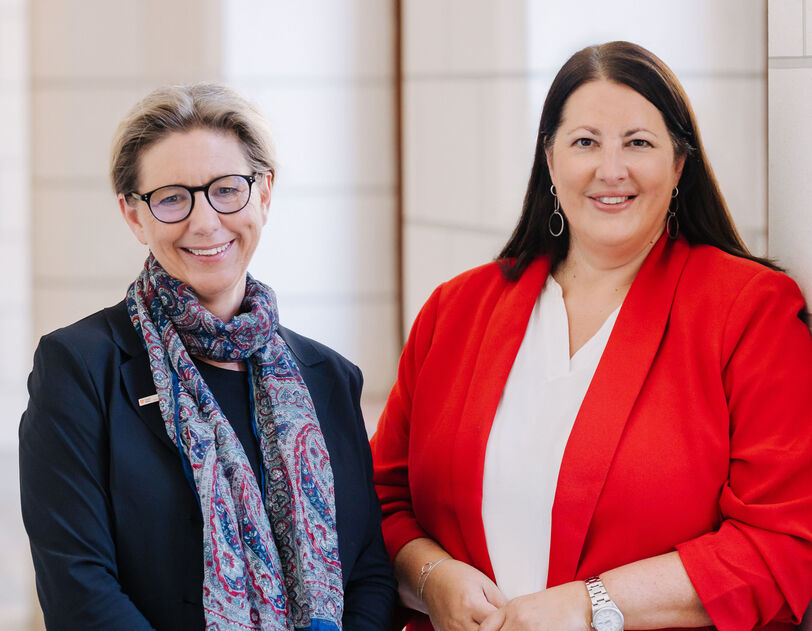 Zwei Frauen, Karin Ramser und Kathrin Gaál, stehen in einem Gang des Rathauses und lächeln in die Kamera. Beide sind businessmäßig mit Blazern gekleidet.