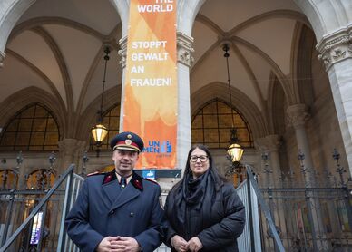 Ein hoher Polizeibeamter in Uniform mit Mantel und die Vizebürgermeisterin im Wintermantel posieren vor der am Wiener Rathaus gehissten orangen Flagge mit der Aufschrift "Orange the World" und "Stoppt Gewalt an Frauen!"